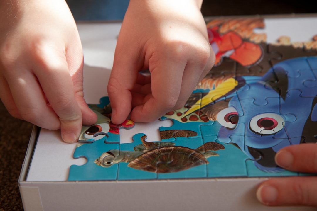Close up of a young boy being helped to assemble a colourful jigsaw puzzle on the carpet at home with his mother
